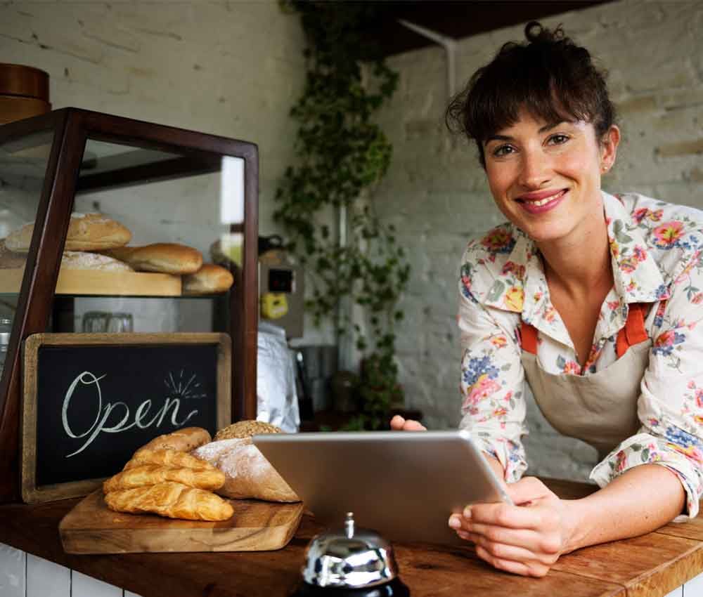 Smiling bakery business owner holding a tablet at the counter with pastries