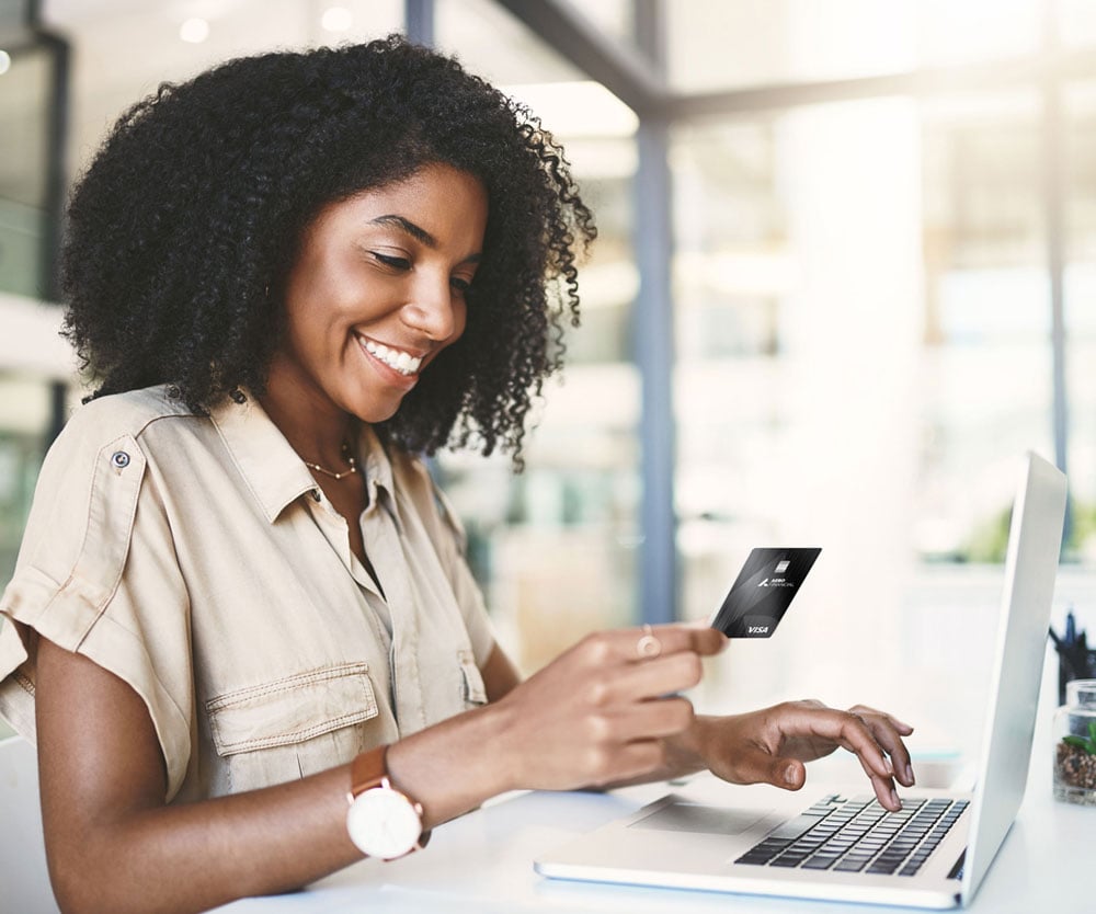 Woman in office holding an AERO business credit card while working on laptop.
