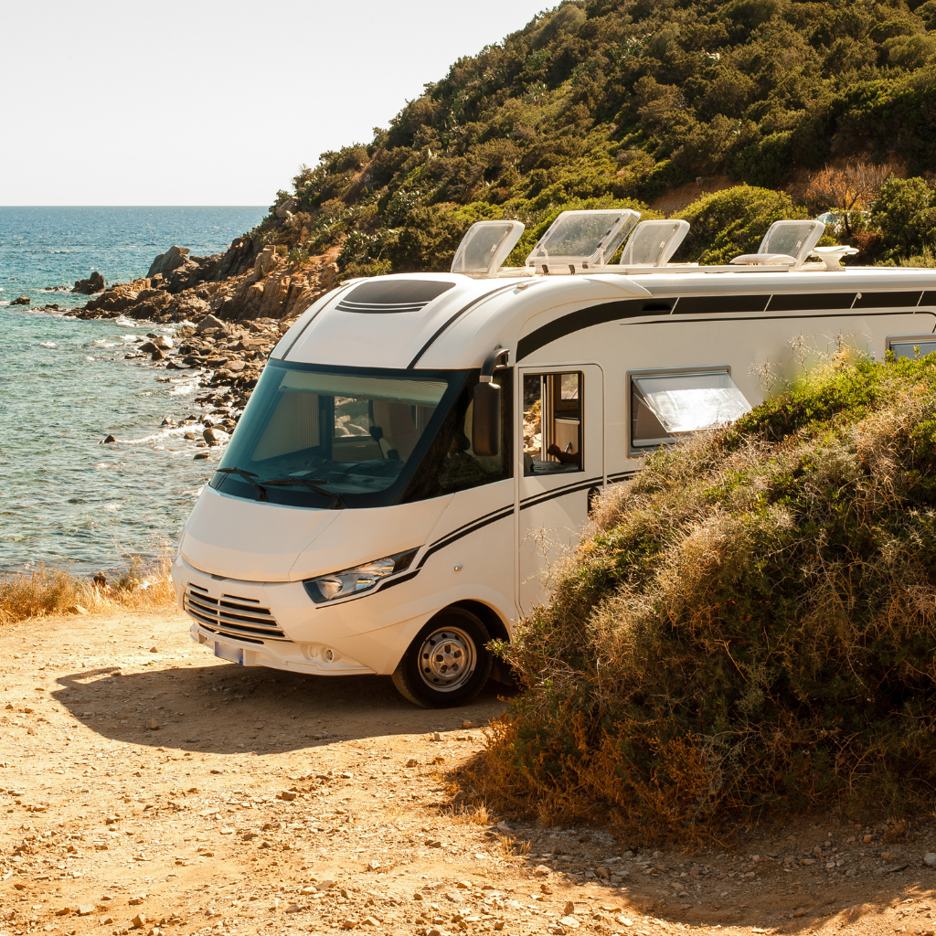 RV parked next to the ocean with mountains in the background