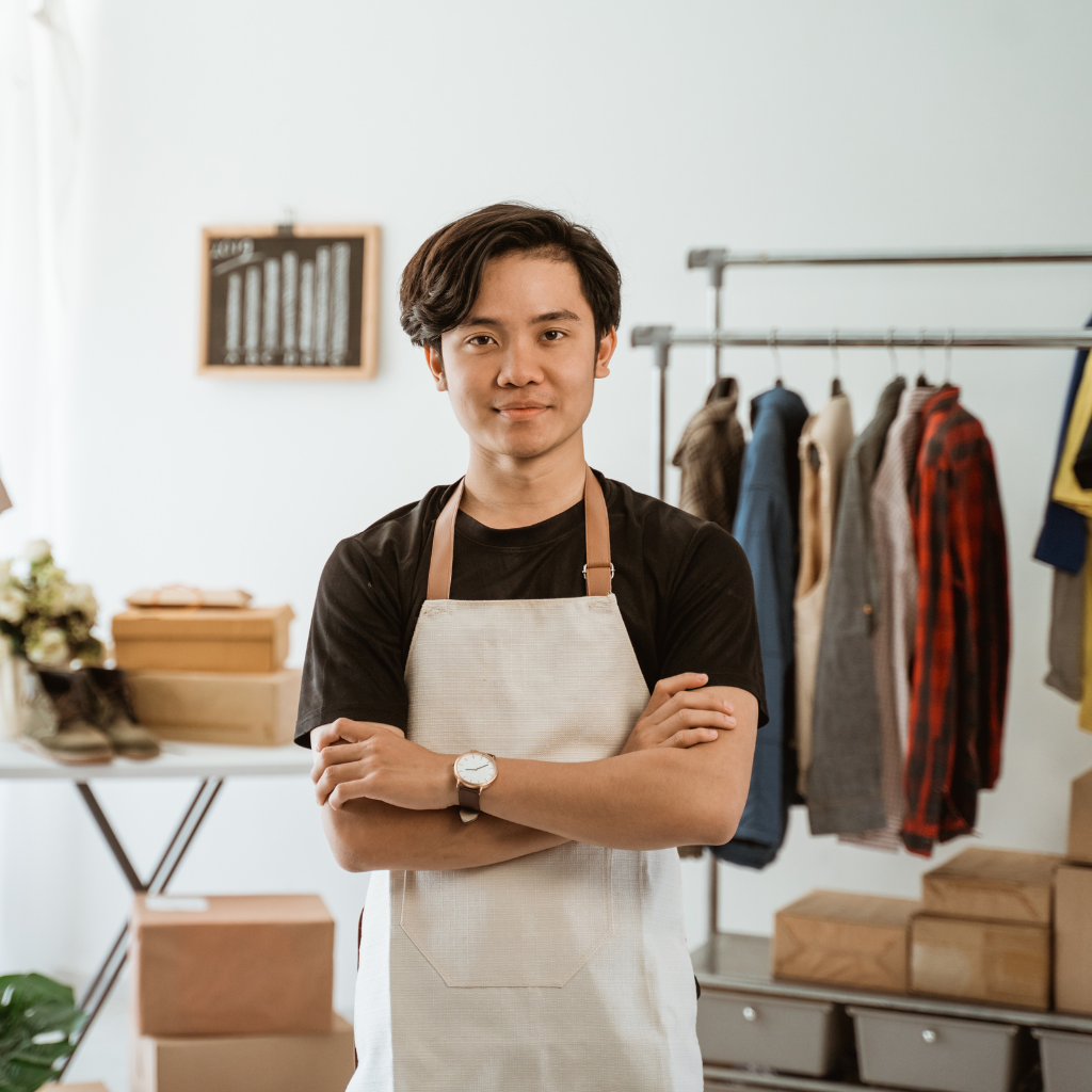 Small business owner wearing an apron with clothing and shipping boxes behind him