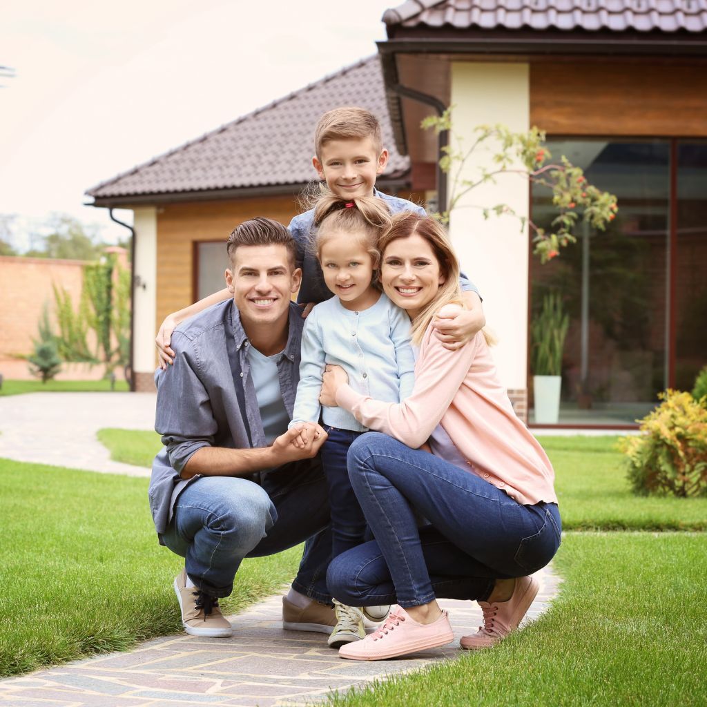 Family kneeling together on front lawn walkway in front of home